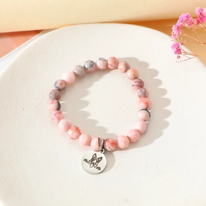 Detail eines rosa Naturstein-Perlenarmbands mit Silber-Hundemotiv auf dem Teller
