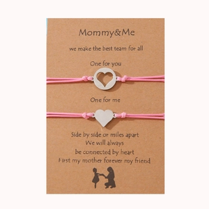 Detalle de dos pulseras trenzadas rosa para madre e hija con dijes de corazón plateados