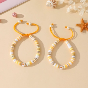 Détail de bracelets ajustables en perles heishi faits main avec cœur sur fond de sable