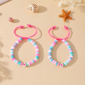 Vue détaillée des bracelets de perles en argile colorées avec motif de cœur sur la plage