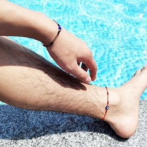 Détail de bracelets Evil Eye tressés rouges et noirs portés au bord de la piscine