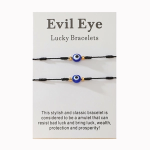 Deux bracelets œil maléfique en corde noire avec perles dorées sur carte de support
