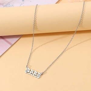 Detailed close-up of a silver angel wings necklace with 999 number pendant on beige marble