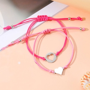 Nahaufnahme rosa geflochtener Armbänder mit Herzanhängern aus Edelstahl auf Strand-Thema