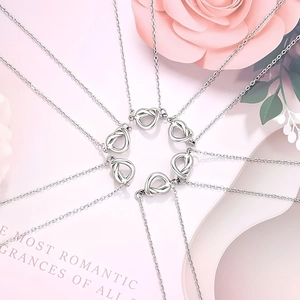 Detalle de seis collares de nudo plateado con colgantes de corazón sobre fondo de rosas