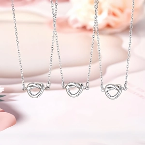 Tres collares de plata con colgante de corazón anudado sobre un fondo floral romántico