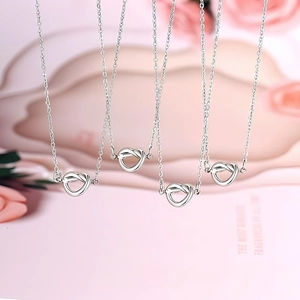 Detalle de collares con colgante de nudo de corazón plateado sobre fondo de rosas rosas
