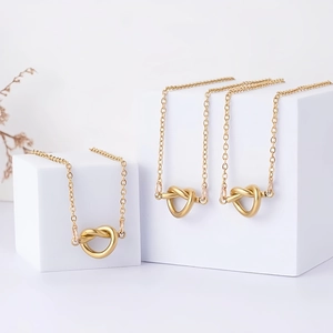 Detalle de tres collares de nudo de corazón dorados en soportes blancos con cadena en O