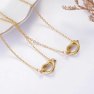 Primer plano del collar dorado con colgante de nudo minimalista y cadena en O pulida