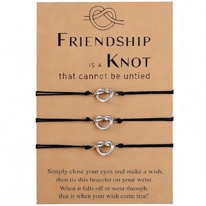 Close-up of three black braided friendship bracelets with silver heart charms on a card