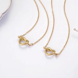 Macro shot of two gold heart knot pendants with polished finish on fine cross chains