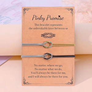 Λεπτομέρεια από βραχιόλια με κόμπο σε κάρτα Pinky Promise με χρυσά και μαύρα κορδόνια