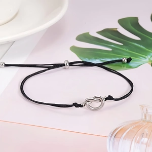 Detail of adjustable black woven bracelet with a silver heart knot charm on soft background