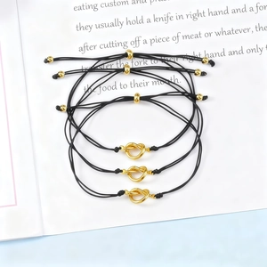 Detail view of three black woven friendship bracelets with gold knot charms on a magazine
