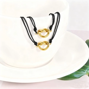 Detail of black woven cord bracelets with golden knotted heart charms on a white ceramic cup