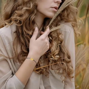 Minimalist black woven rope bracelet with gold heart knot pendant worn by model outdoors
