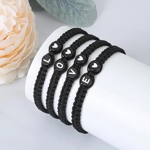 Detailopname van de zwarte gevlochten LOVE-armband op een witte standaard met bloemen