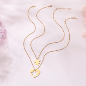 Détail de l'ensemble collier cœur et pièce de puzzle dorés sur fond rose pastel