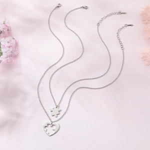 Détail de colliers en forme de cœur puzzle argentés sur fond rose clair