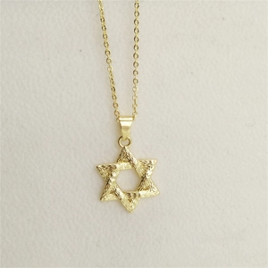 Macro detail of gold hexagram star necklace with textured surface and dainty cross chain