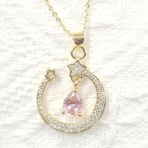 Macro shot of gold moon and star necklace with pink teardrop crystal and zircons