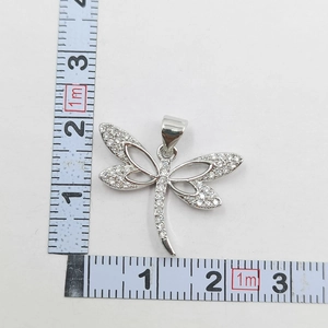 Detailed view of silver dragonfly pendant with micro-inlaid zircons next to a ruler