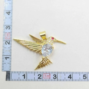 Detail of gold hummingbird pendant with pear-cut stone and measuring tape for size scale
