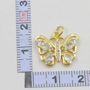 Macro shot of gold-plated butterfly pendant with cubic zirconia next to a measuring tape