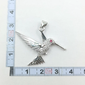 Macro view of a silver hummingbird pendant with white crystals and red gemstone eye