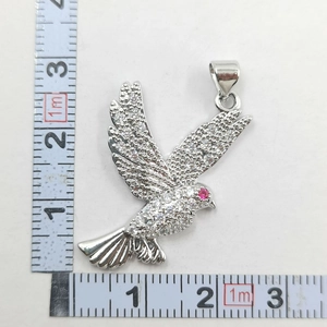 Detailed view of a silver bird pendant with white zircons and a ruby eye near a tape measure