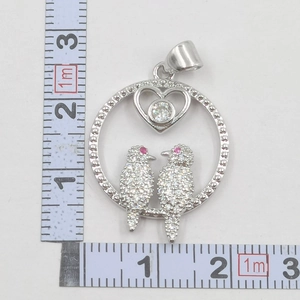 Detail shot of a round silver bird pendant with heart motif and size scale reference