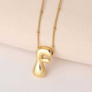 Nahaufnahme des polierten goldenen 3D-Buchstaben F Anhängers mit eleganter Kugelkette