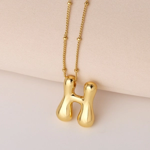 Nahaufnahme des goldenen H-Buchstabenanhängers im Ballonstil mit Perlenkette