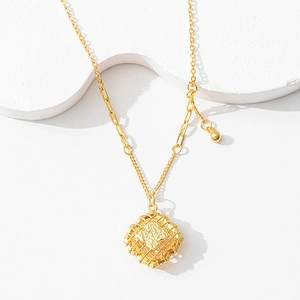 Detail view of hollow geometric gold pendant with CNC embossed texture on mixed chain