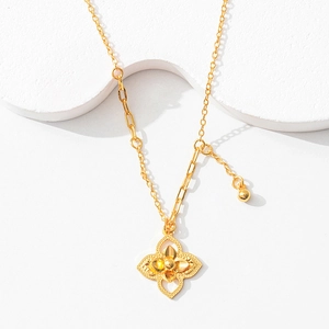Detail of gold four-petal flower pendant with unique asymmetrical chain on a white stand