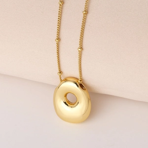 Detailaufnahme eines polierten goldenen Donut-Anhängers an einer feinen Perlenkette
