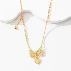 Close-up of gold bow necklace with heart pendant and textured diamond pattern chain