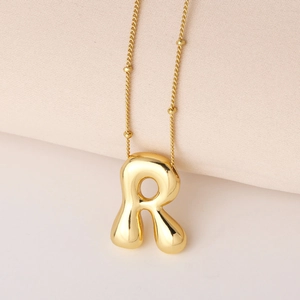 Makro-Detail eines goldenen 3D-Buchstaben-R-Anhängers mit einer goldenen Kugelkette