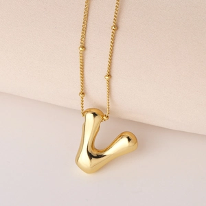 Makroaufnahme des polierten goldenen Buchstaben V Anhängers mit 3D-Chunky-Design