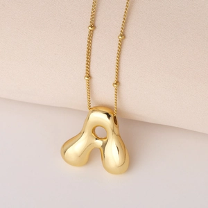 Minimalistische goldene Kette mit A-Initial-Anhänger und Perlenkette auf Stoff