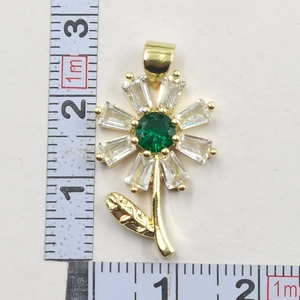 Macro shot of gold sunflower pendant with green stone next to measuring scale