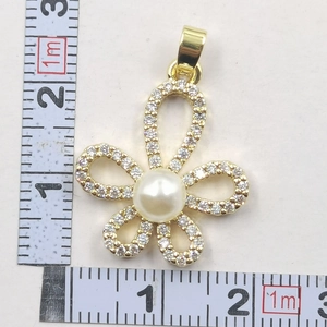 Detail view of sunflower clover pendant with white pearl and pave crystals next to a ruler