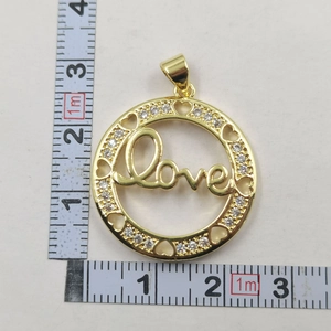 Close-up of golden Love pendant with white zircon inlays and ruler for size scale