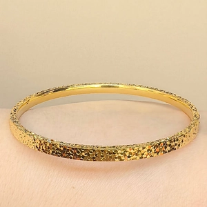 Nahaufnahme eines goldbeschichteten Armreifs mit glitzernder Oberfläche und Textur für Damen