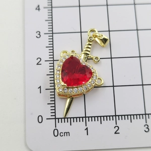 Detail view of heart and dagger pendant with red stone on a metric measurement scale