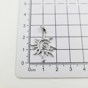 Macro shot of silver sun pendant with spiral texture and zircon on a measuring board
