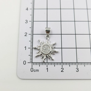 Detailed measurement of silver sun pendant with rhinestones on a metric grid ruler