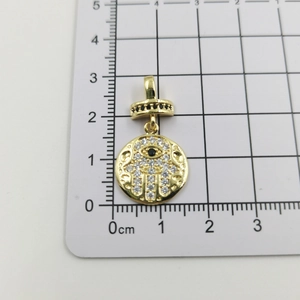 Detailansicht der goldenen Hamsa-Anhänger mit weißem Zirkon und schwarzem Stein auf Skala