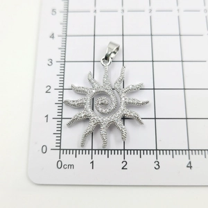 Detailed view of silver sun flower pendant with sparkling crystals on measurement grid