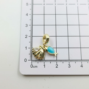Detailansicht eines Gold-Muschelanhängers mit blauem Tropfen auf einem Linealmaßstab